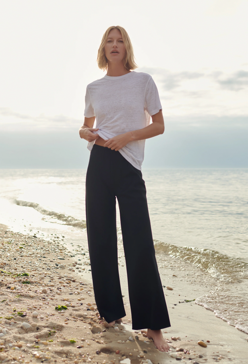 a model wearing black pants and a linen white t-shirt at the beach.