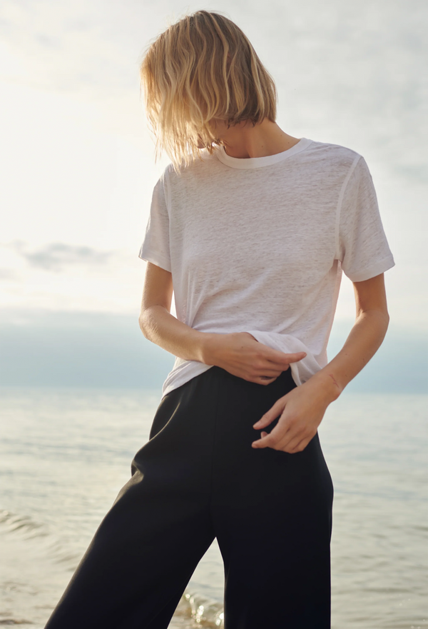 a model wearing black pants and a linen white t-shirt at the beach.