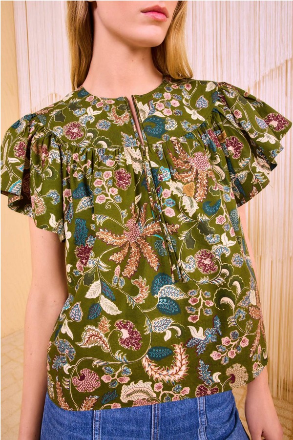 Closeup photo of the green floral printed shirt. The high waisted jeans are visible and the photo is taken with a fringe background. 