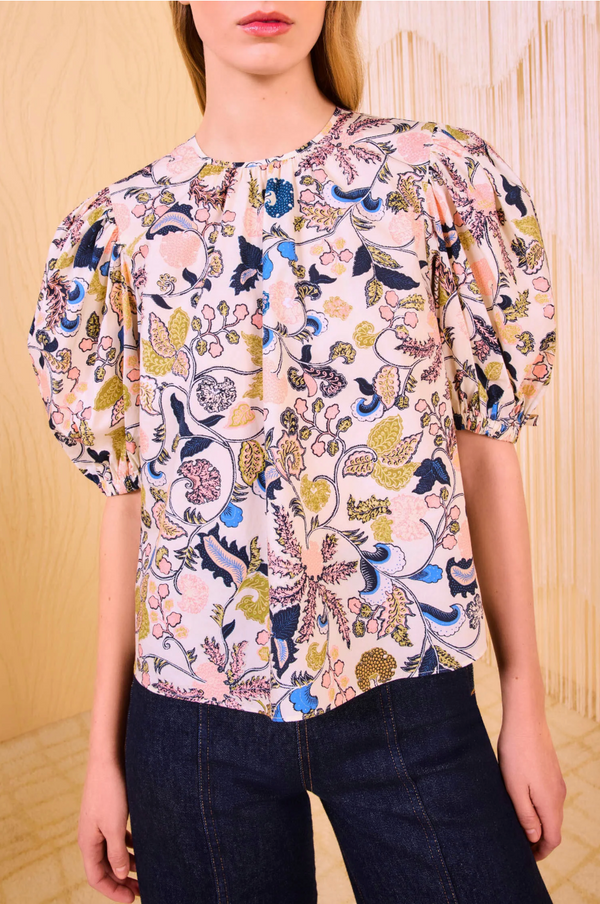 Closeup photo of the model's top, which is a white base floral with green blue and pink floral motifs. The model is wearing dark wash high waisted jeans. 