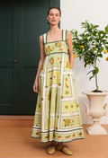 Woman wearing a floral dress standing indoors with a plant in the background