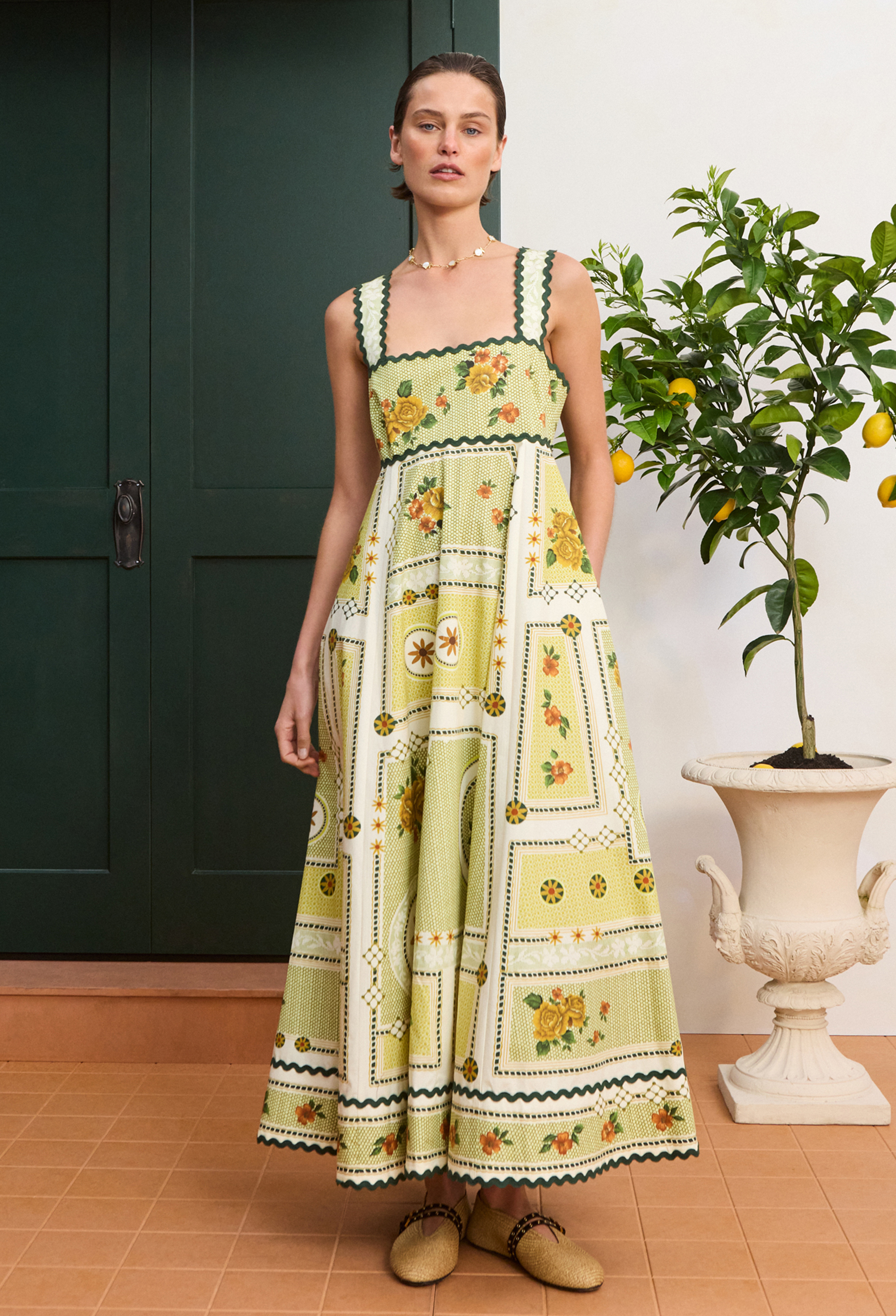 Woman wearing a floral dress standing indoors with a plant in the background