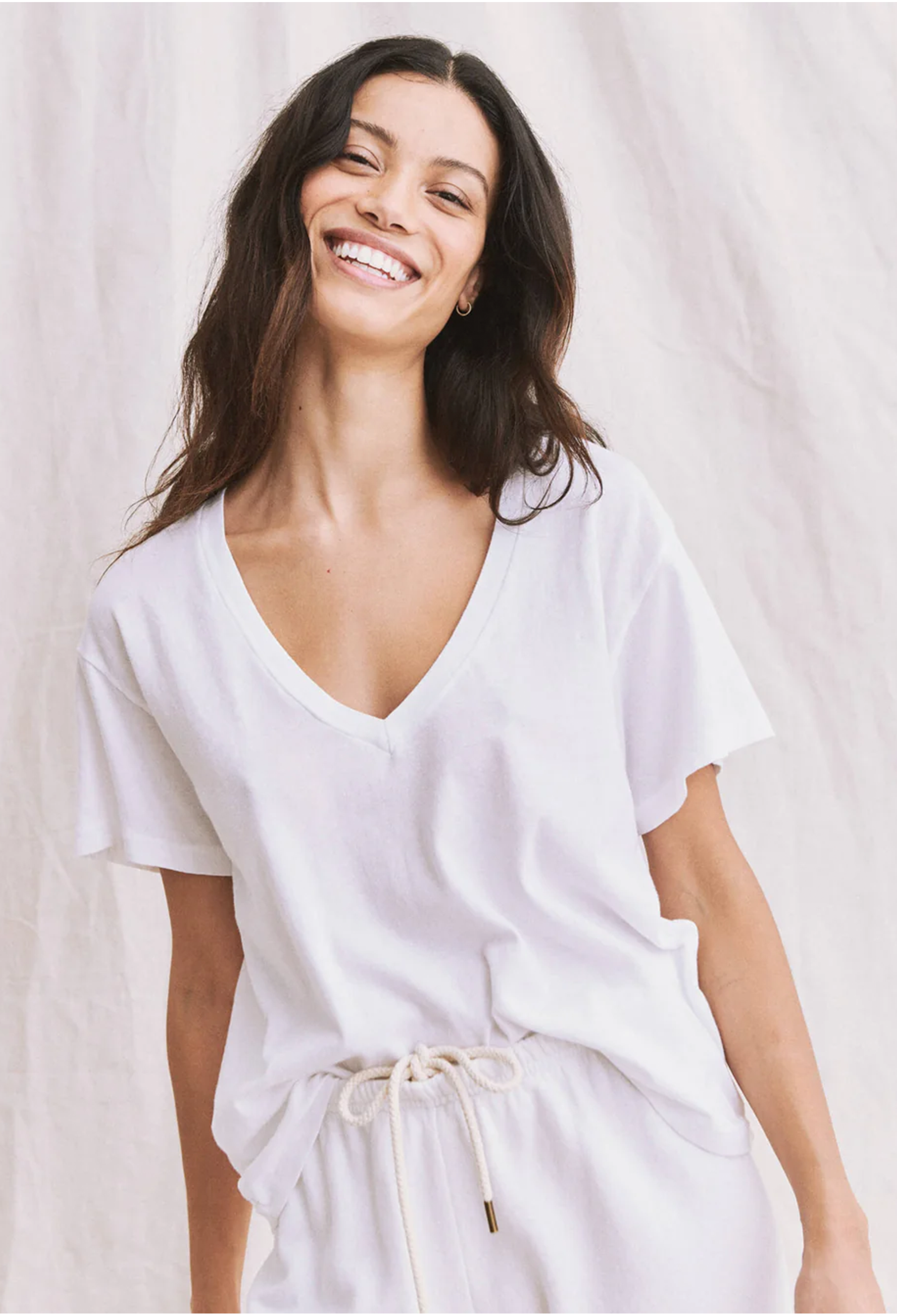 a woman wearing a white v-neck t-shirt tucked into white sweats. white background