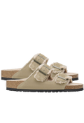 Pair of beige double strap sandals with shearling inside and gold buckles. Set against a checkered background. 