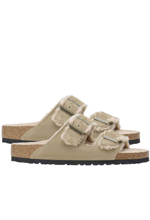 Pair of beige double strap sandals with shearling inside and gold buckles. Set against a checkered background. 
