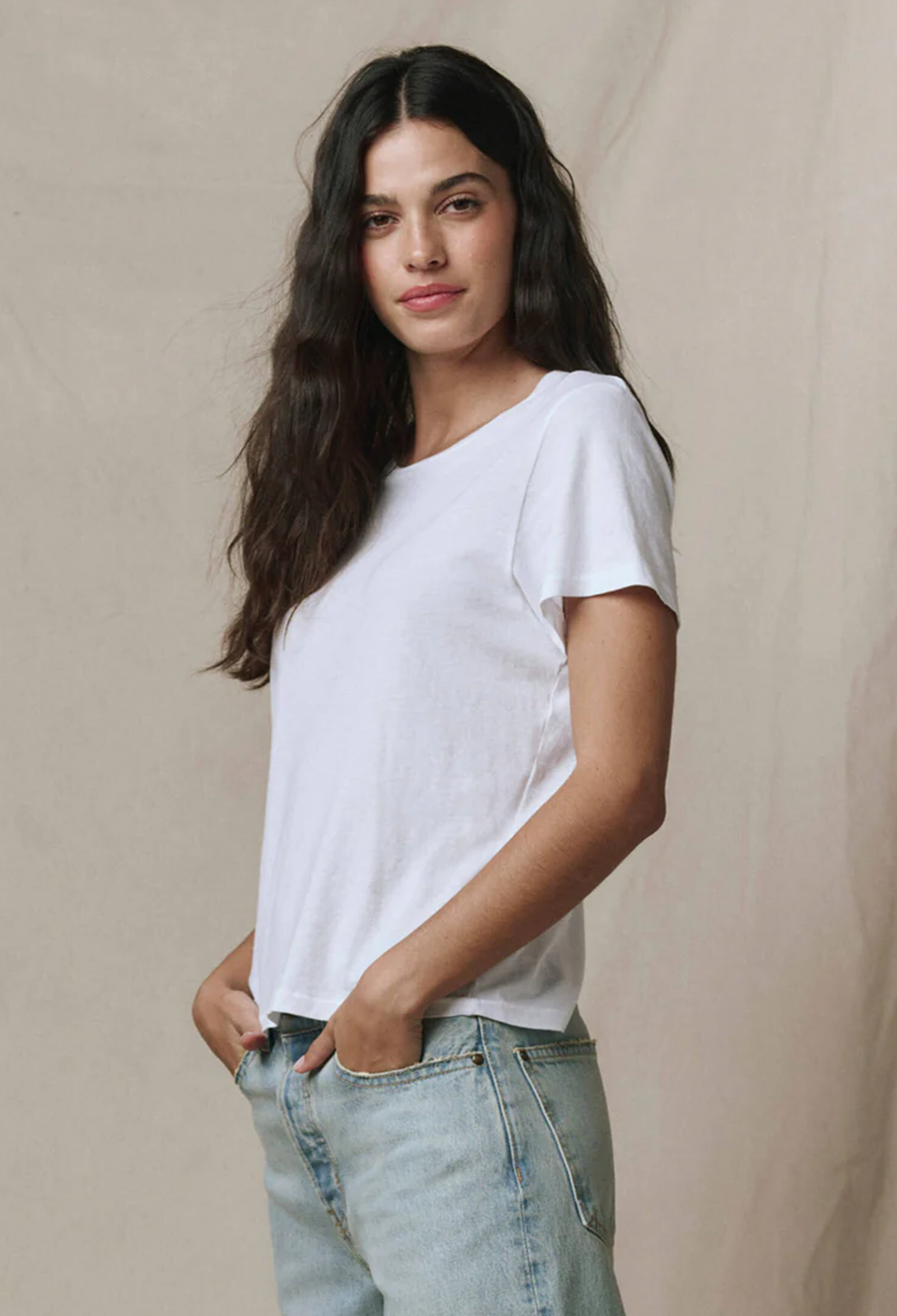 Woman wearing a white t-shirt and light blue jeans against a beige background