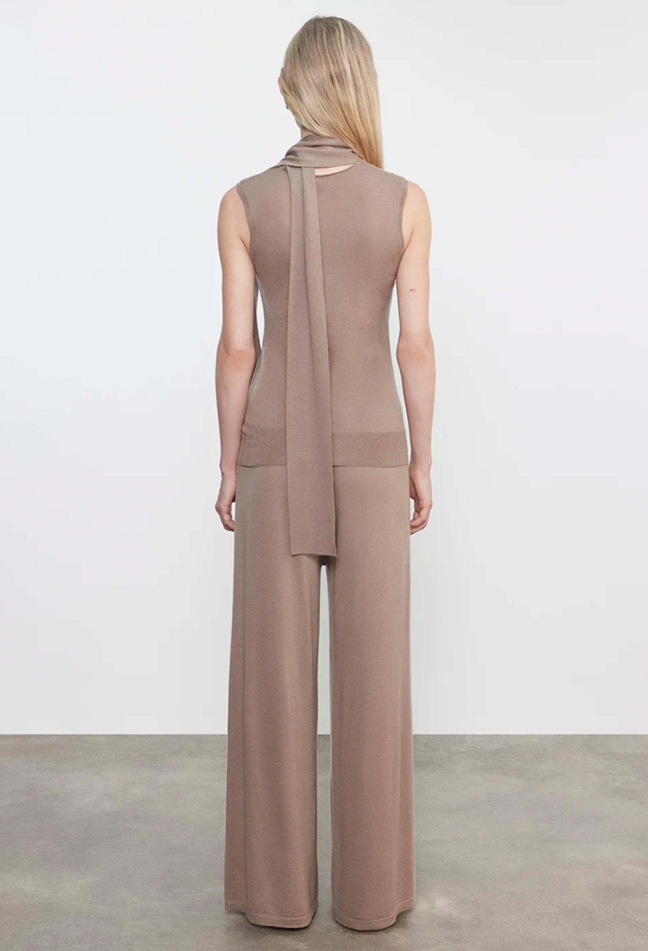 Woman wearing a beige sleeveless top and wide-leg pants on a plain background