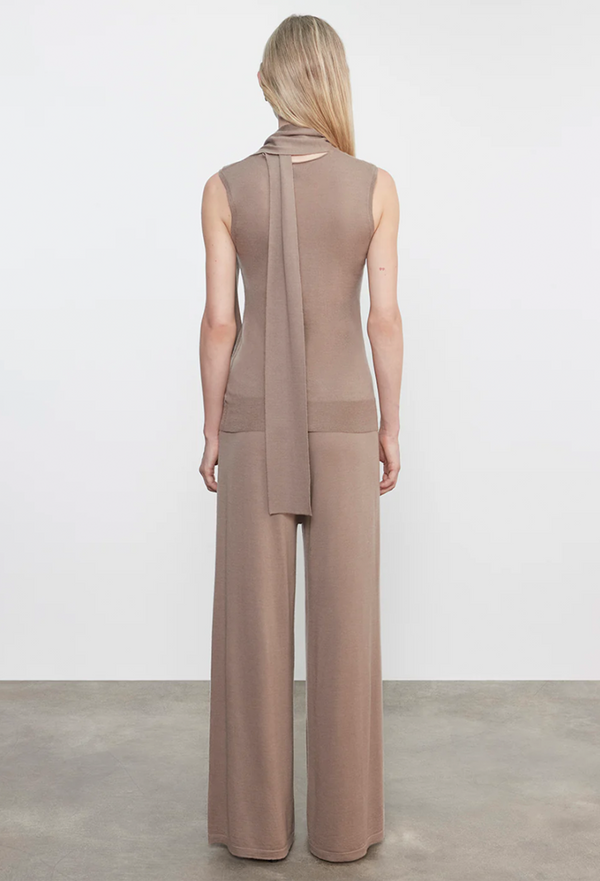Woman wearing a beige sleeveless top and wide-leg pants on a plain background