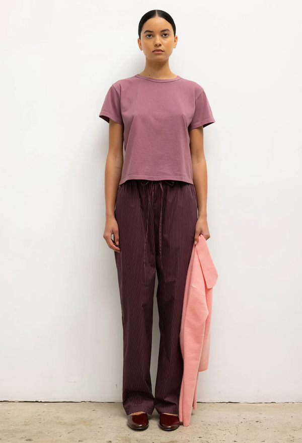 Woman wearing a mauve top and brown pants holding a pink garment against a white background