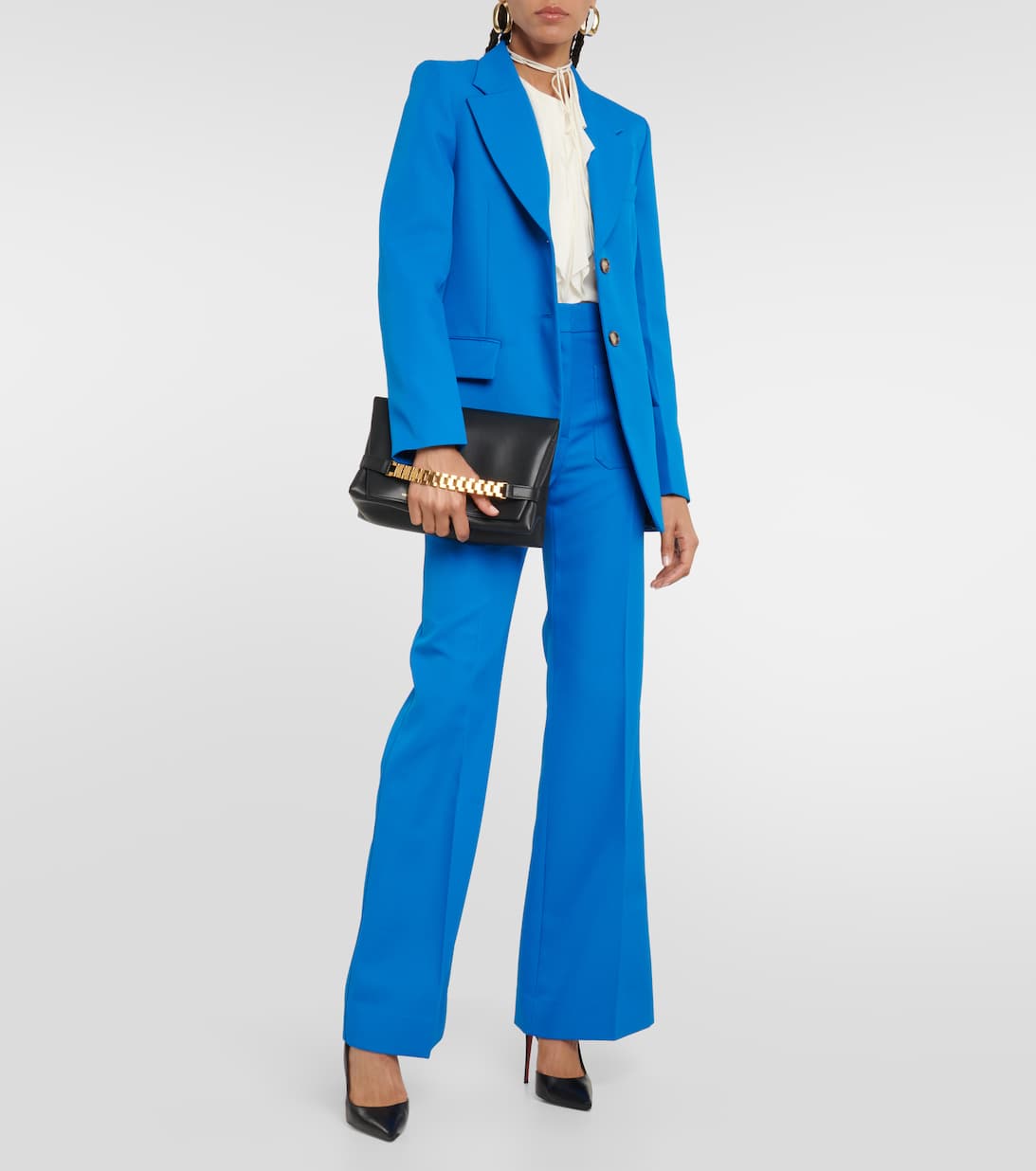 Model wears blue blazer with matching blue pant and white blouse underneath. She carries a black purse with gold handle, and wears black heels. 