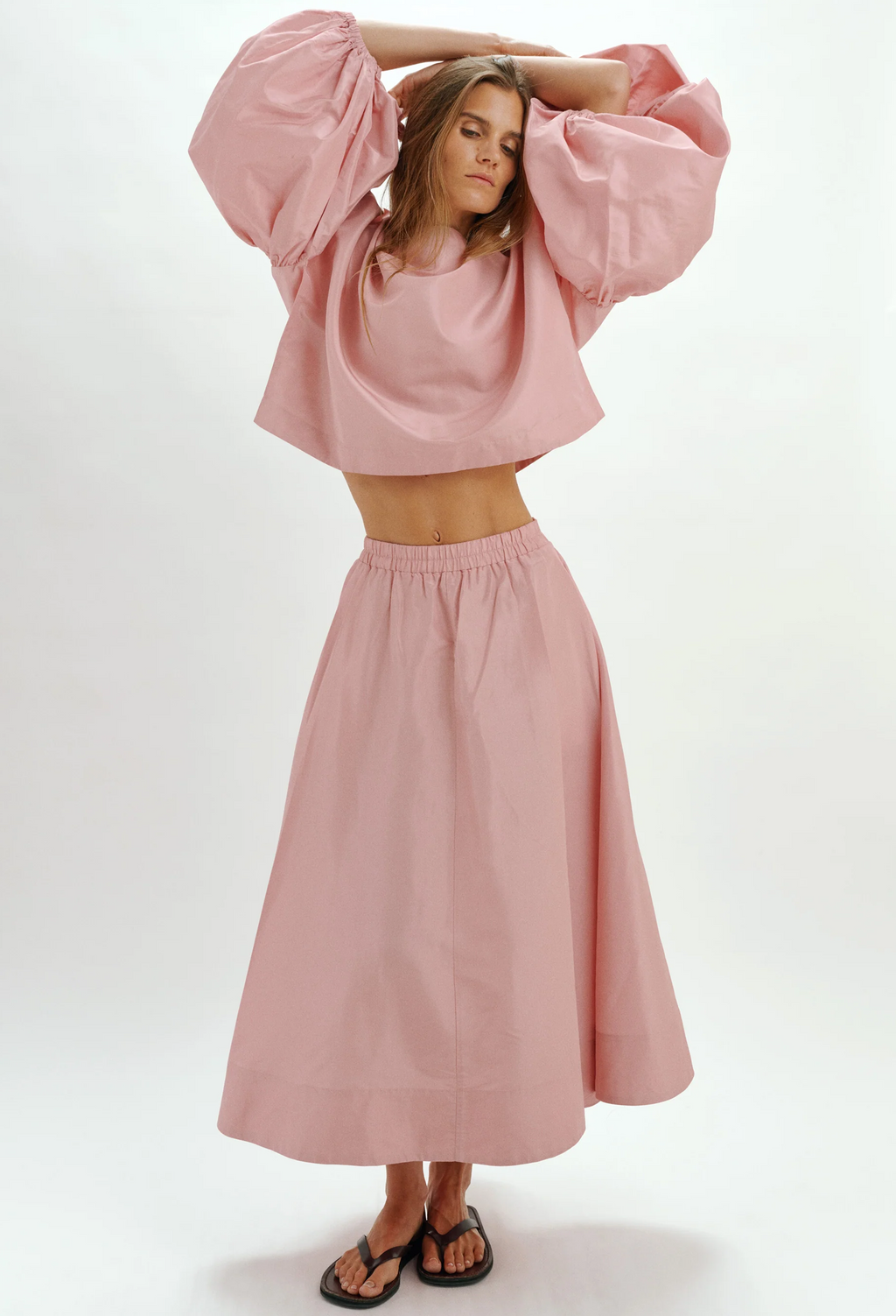 Woman wearing a pink outfit with a top and long skirt on a white background