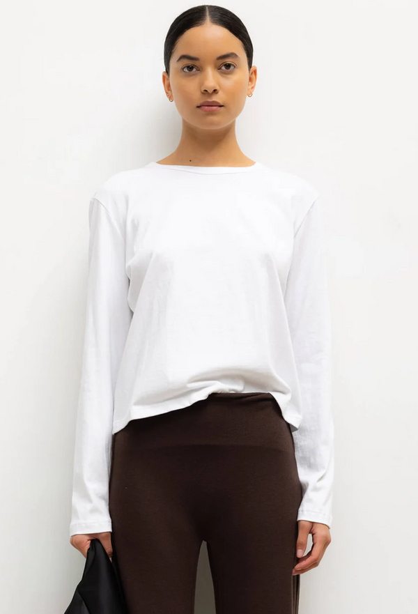 Woman wearing a white long-sleeve top and brown pants against a white background