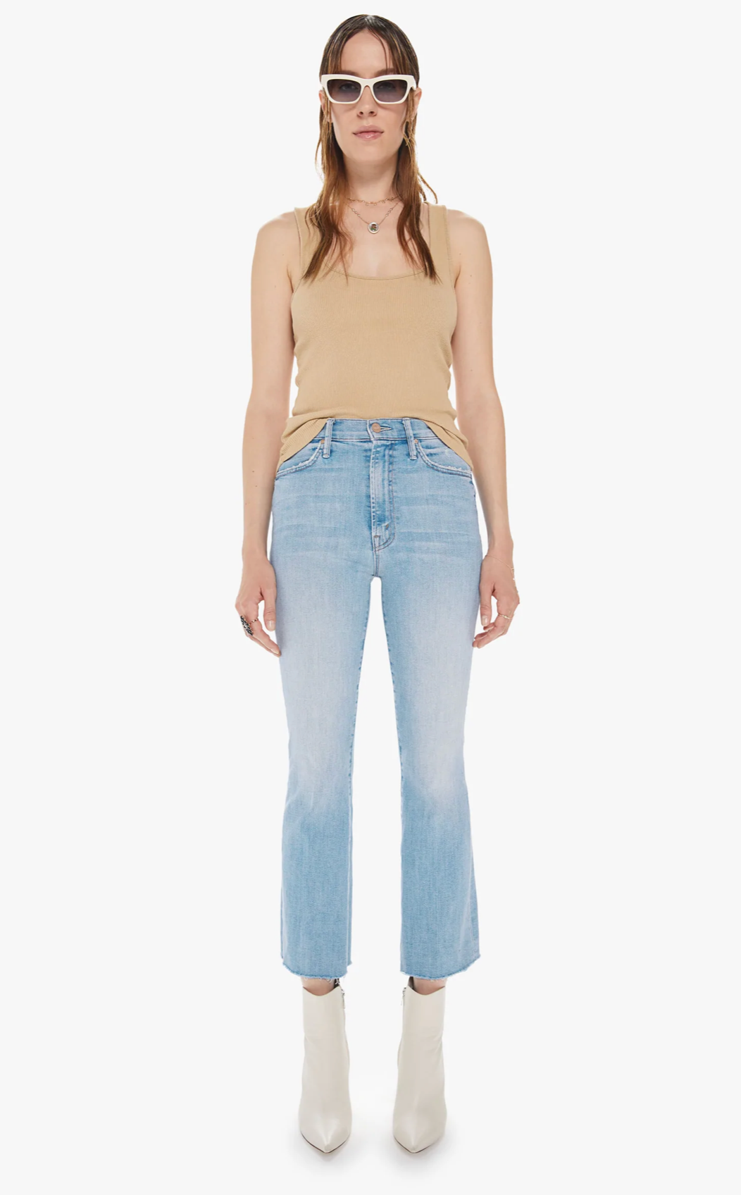 Model wears cropped light wash jean with white boots, tan tank top, and white sunglasses. Set against a white background.